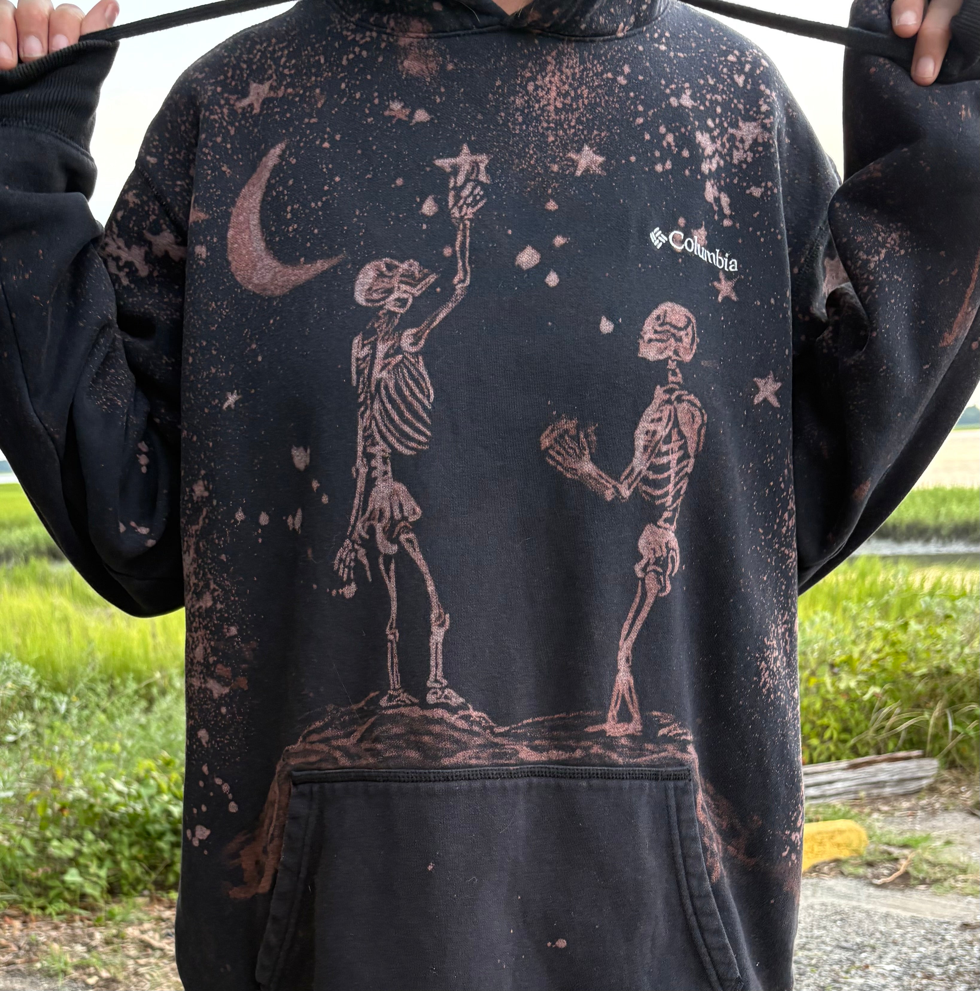 Black hoodie with skeleton and stars design worn by a person outdoors