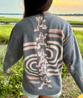 Person wearing a gray bleach art sweatshirt with frog and unique line designs as well as swirly smiley faces 