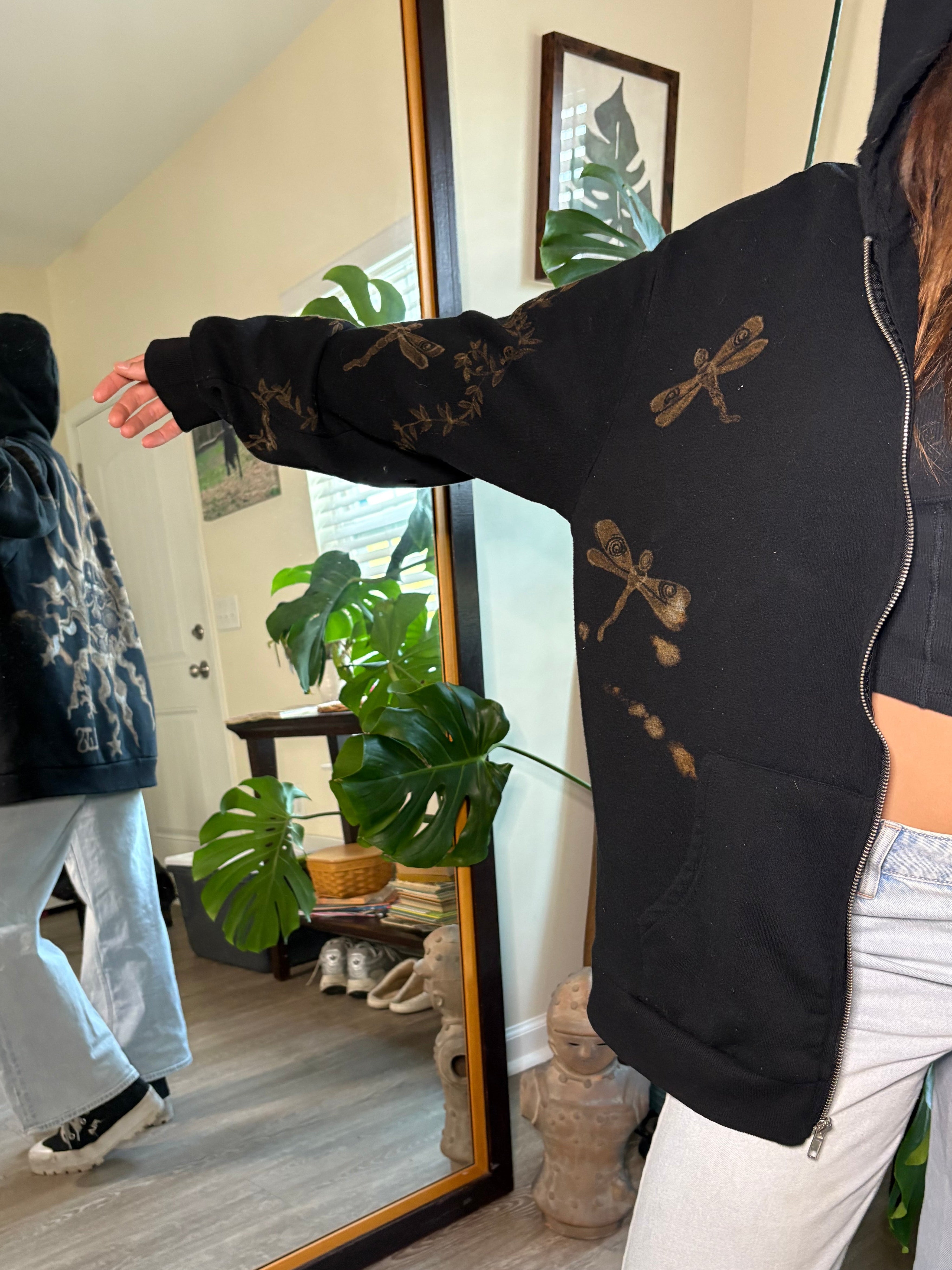 Person wearing a black sweatshirt with bleach art dragonflies designs on the front of a zip up jacket 