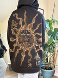 Person wearing a black hoodie with bleach art sun with butterflies design on the back in a room with plants.