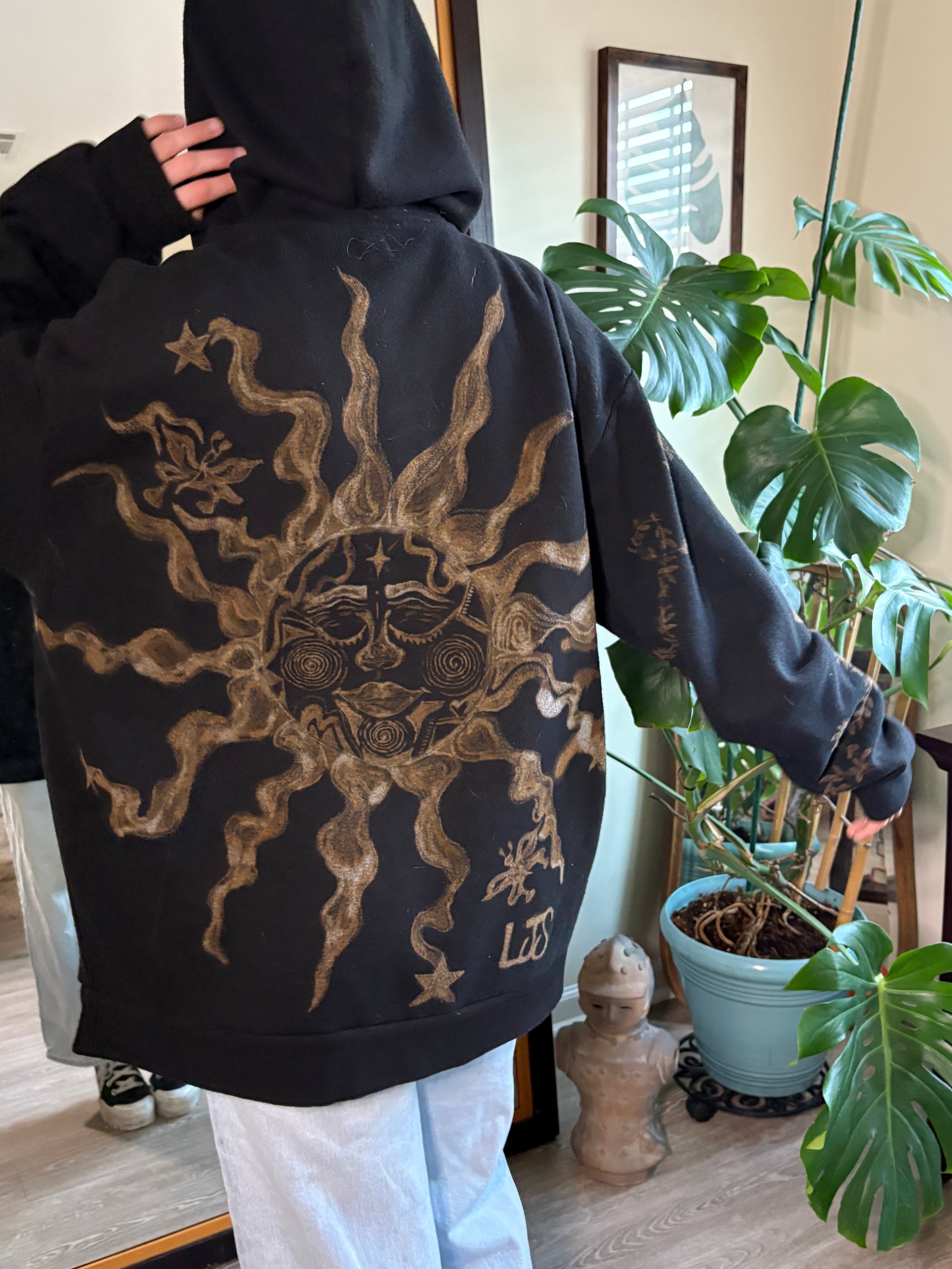 Person wearing a bleach art black hoodie with a sun face and butterflies 